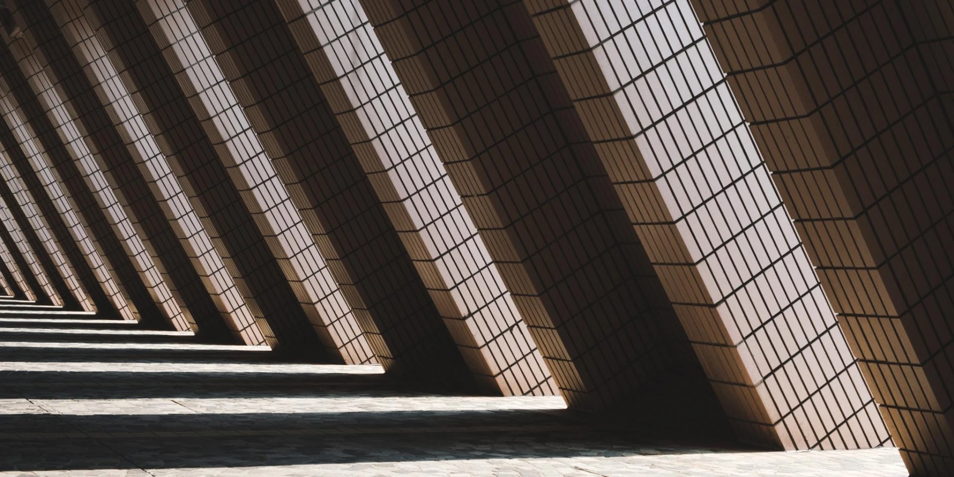 A series of angled columns casting dramatic shadows across a textured floor, creating a geometric pattern with strong contrast between light and dark.