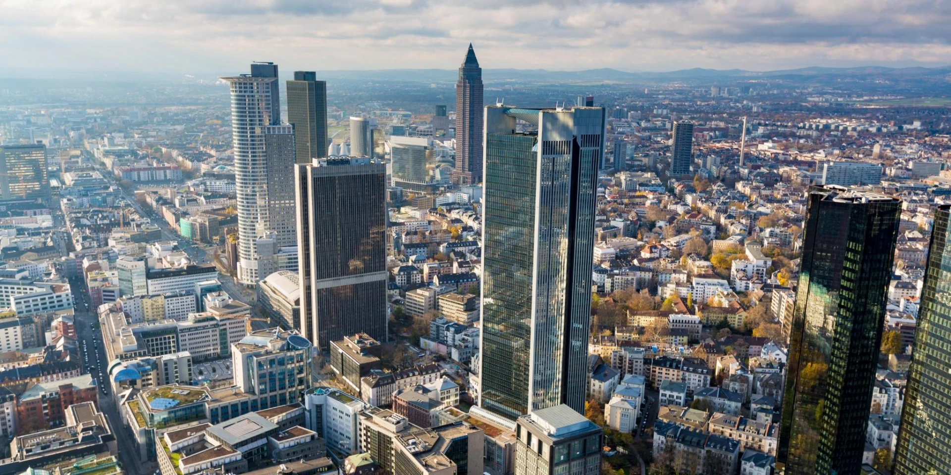 An aerial view of Frankfurt, Germany, highlighting its modern skyscrapers, including the Deutsche Bank towers and Commerzbank Tower, amidst a sprawling urban cityscape.